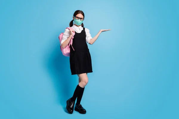 Full size photo of high school girl in medical mask hold hand recommend promotion advertisement wear rucksack white blouse black rock dress long socks isolated over blue color background — Stockfoto