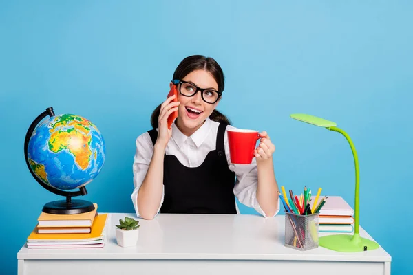 Positivo de la escuela secundaria chica sentada mesa tienen lección descanso bebida taza bebida uso smartphone llamada amigo decir decir académico noticias desgaste blanco blusa negro en general aislado azul color fondo — Foto de Stock