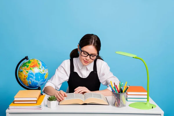 Foto de estudiante de secundaria concentrada niña sentarse mesa leer libro de texto atento tienen cursos académicos académicos usan blusa blanca negro uniforme general aislado color azul fondo — Foto de Stock