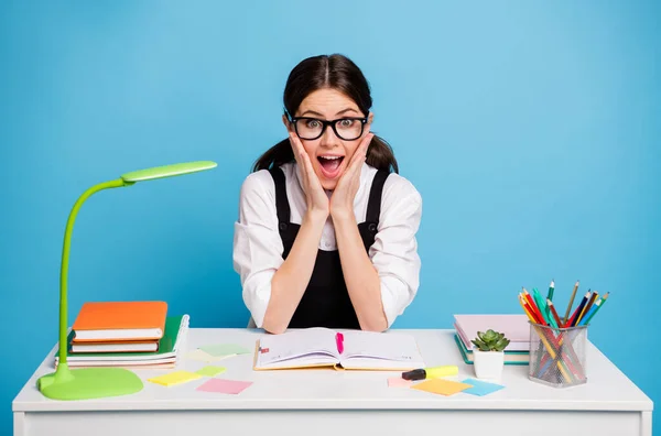 Foto de chica loca asombrada de la escuela secundaria sentarse mesa escribir trabajo en casa impresionado buenas calificaciones académicos cursos usan blusa blanca negro uniforme general aislado color azul fondo —  Fotos de Stock