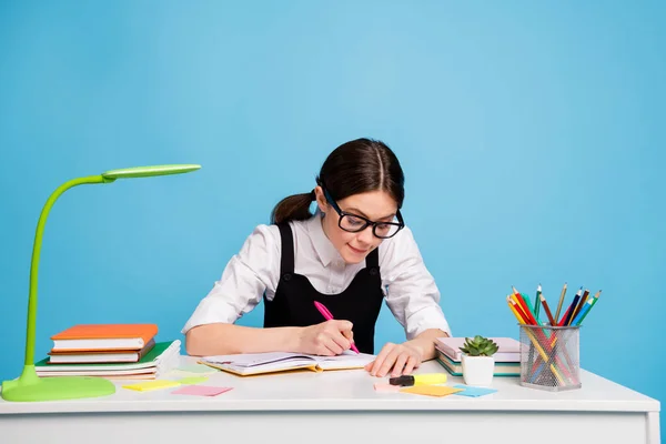 Foto de chica concentrada inteligente sentarse mesa escribir copybook proyecto de la escuela secundaria ropa blanca negro elegante uniforme de moda en general aislado sobre fondo de color azul — Foto de Stock