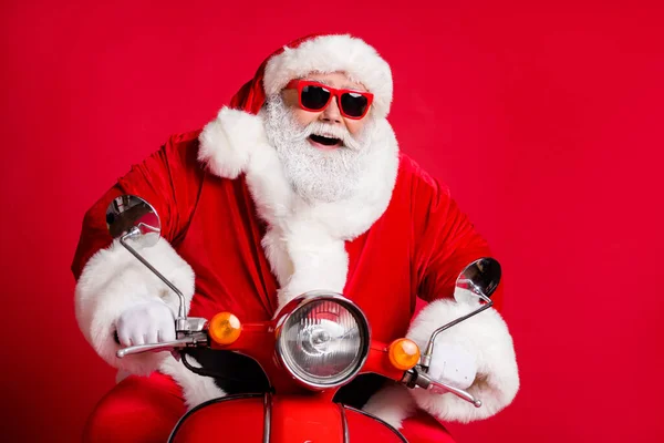 Foto de aposentado vovô branco barba passeio retro ciclomotor confiante despreocupado sentir vento rosto condução pressa natal evento desgaste x-mas traje casaco sol vidro tampa isolado vermelho cor fundo — Fotografia de Stock