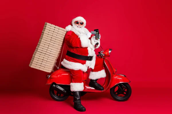 Profilo completo foto di nonno in pensione retro scooter pizza box tenere carta di credito contactless servire cliente terminale usura x-mas costume cappotto di occhiali da sole tappo isolato colore rosso sfondo — Foto Stock