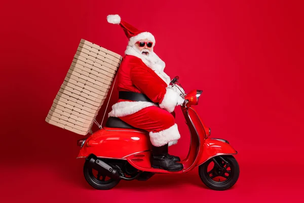 Pełna długość profil zdjęcie emerytowanego dziadka biała broda jeździć vintage motorower pizzy pudełka Boże Narodzenie dobroczynność dostawy nosić Santa X-mas kostium płaszcz czapka okulary przeciwsłoneczne izolowane czerwony kolor tło — Zdjęcie stockowe