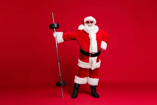 Full body size zdjęcie emeryta biały broda trzymać sztanga pewnie rozgrzewanie siłownia nosić Santa X-mas kostium płaszcz okulary skórzane buty odizolowany czerwony kolor tło — Zdjęcie stockowe