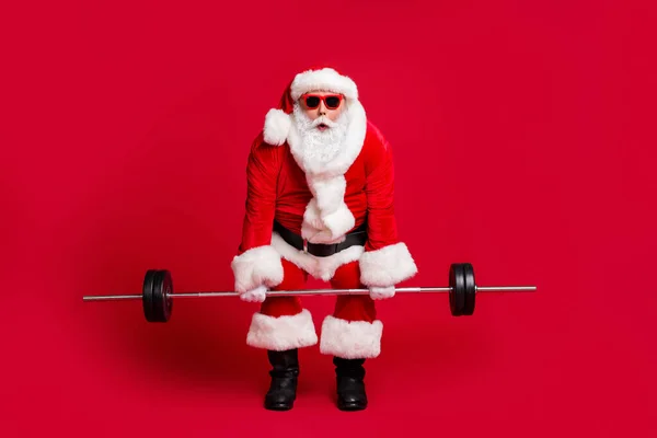 Too heavy. Full length photo of retired old man white beard hold barbell shocked look almost drop wear x-mas santa costume glove coat belt sunglass cap boot isolated red color background — Stock Photo, Image