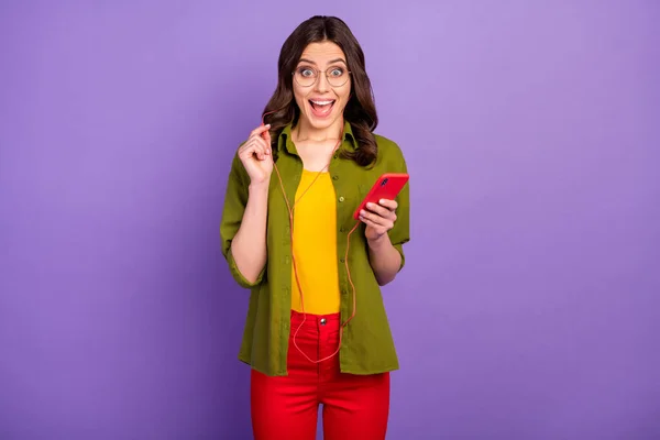 Retrato de chica positiva sorprendida uso smartphone escuchar increíble radio melodía auriculares impresionados grito wow omg desgaste estilo elegante moda auriculares aislados color violeta fondo — Foto de Stock