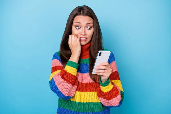 Foto van bang blogger meisje gebruik smartphone lezen verschrikkelijk verschrikkelijk social media nieuws bijten vingers tanden dragen regenboog stijl trui geïsoleerd over blauwe kleur achtergrond — Stockfoto