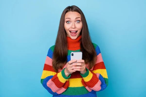 Foto de menina surpreso louco usar smartphone viciado blogging impressionado rede social feedback desgaste arco-íris estilo suéter isolado sobre azul cor de fundo — Fotografia de Stock