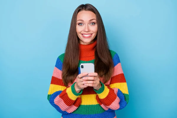 Portret pozytywnej wesołej dziewczyny blogger korzystać smartfon korzystać social media pisania akcji repost aktualności nosić tęczowy sweter odizolowany na tle niebieskiego koloru — Zdjęcie stockowe
