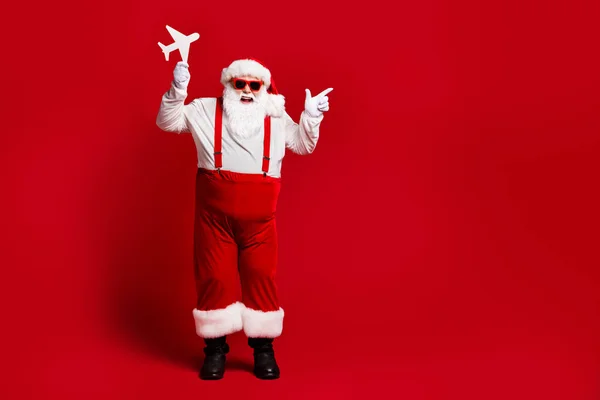Pleine longueur de la taille du corps vue de son il attrayant joyeux joyeux joyeux Père Noël tenant dans les mains avion en papier montrant l'espace de copie isolé brillant vif vibrant rouge bordeaux fond de couleur marron — Photo