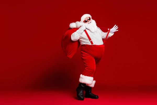 Повна довжина тіла погляд на його привабливу дитину веселий веселий веселий жир Санта, що несе великий мішок, розважаючись, танцює ізольовано яскраво-світлий яскравий червоний колір фону — стокове фото