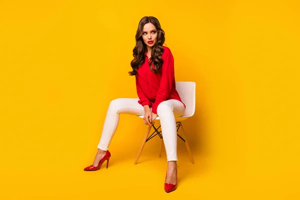 Полное фото тела привлекательной шикарной деловой леди сидеть стул кокетливый взгляд боковое пространство позирует фотограф носить красную рубашку белые брюки на высоких каблуках изолированные желтый яркий цвет фона — стоковое фото