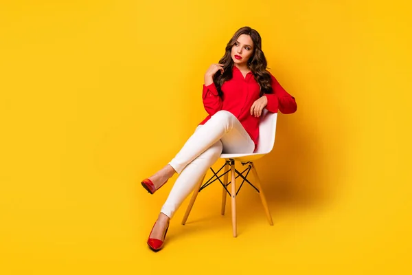 Foto em tamanho completo de atraente senhora de negócios sentar cadeira confortável pessoa séria olhar lado vazio espaço desgaste vermelho escritório camisa branco calças de salto alto isolado amarelo cor viva fundo — Fotografia de Stock