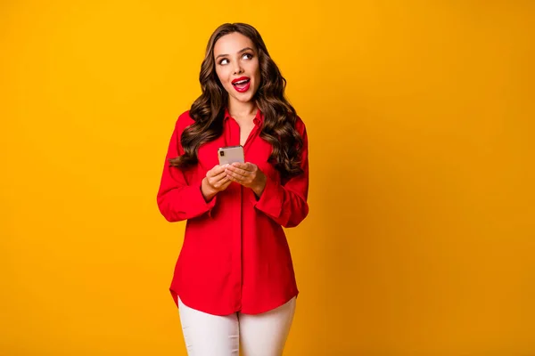 Foto de atraente muito ondulado senhora segurar as mãos do telefone olhar lado espaço vazio ver anúncio banner desgaste vermelho escritório camisa branco calças isoladas amarelo vibrante cor fundo — Fotografia de Stock