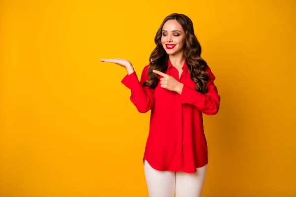 Foto van mooie zakelijke dame houd open hand lege ruimte bieden nieuwigheid product directe vinger arm verkoop prijzen dragen rood kantoor shirt witte broek geïsoleerde geel heldere kleur achtergrond — Stockfoto