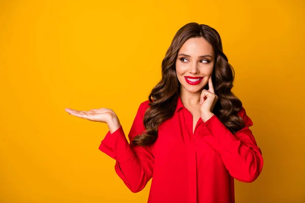 Foto de atractiva señora de negocios bastante rizado mantenga la mano abierta gerente de ventas de espacio vacío mostrando novedad producto desgaste camisa de oficina roja aislado amarillo vibrante color fondo —  Fotos de Stock