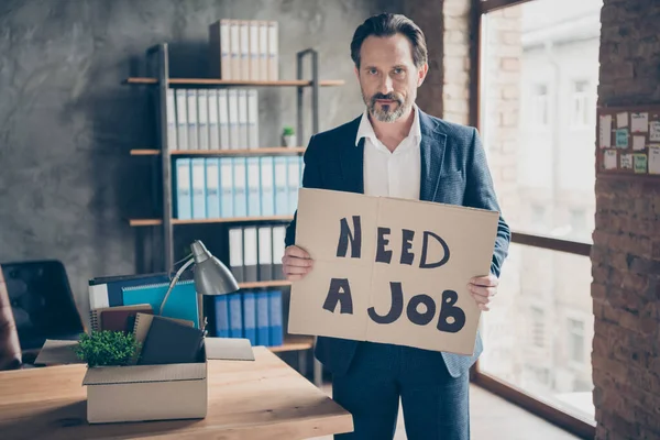 Portré az ő komoly munkanélküli srác ingatlanügynök közgazdász tartja a kezében placard mondván szüksége van egy munkát találni megoldás a modern loft ipari tégla stílusú belső munkaállomás — Stock Fotó