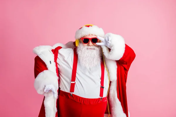 Cool funky cheveux blancs gris barbe Père Noël claus gros abdomen écouter x-Noël Noël radio chansons écouteurs essayer de danser faire signe v porter lunettes de soleil serre-tête bretelles isolé fond de couleur pastel — Photo