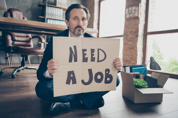 Retrato dele ele deprimido banqueiro cara desempregado sentado no chão de madeira segurando cartaz precisa de um emprego palavras implorando novo local de trabalho no loft moderno estilo tijolo industrial estação de trabalho interior — Fotografia de Stock