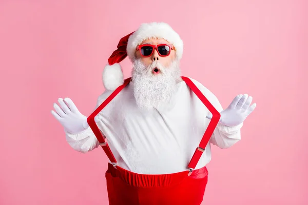 Bild av förvånad övervikt Tomten imponerade tradition x-mas jul shopping försäljning nyheter dra hängslen bära huvudbonad overall solglas isolerad rosa färg bakgrund — Stockfoto