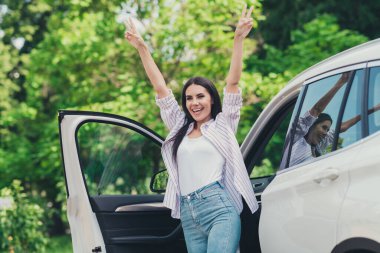 Photo of excited girl enjoy buying new private car rejoice make v-sign cant wait drive ride in town center outside clipart