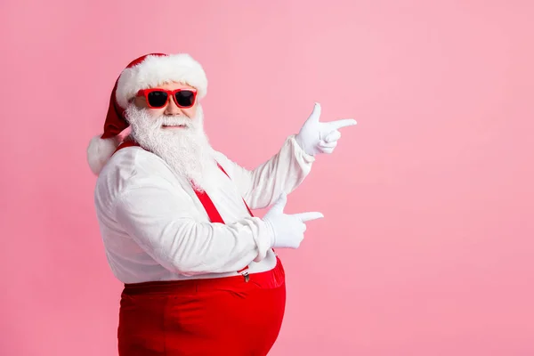 Profilseite Foto von lustig Fett übergewichtig Weihnachtsmann zeigen Zeigefinger Copyspace X-mas Werbung tragen Overalls Hosenträger Kopfbedeckung Sonnenbrille isoliert über pastellfarbenem Hintergrund — Stockfoto