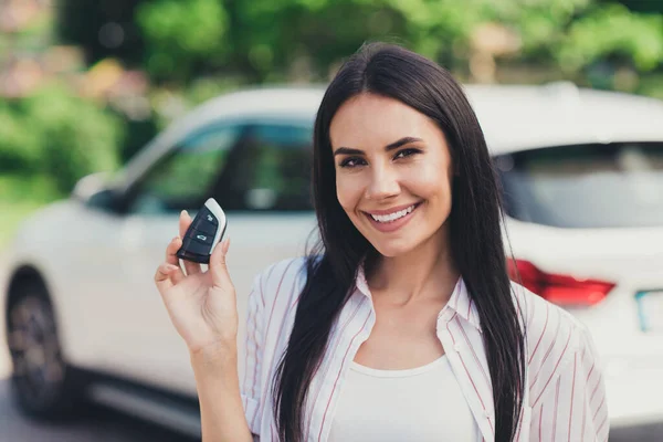 Close-up portrait of her she nice attractive pretty lovely cute content cheerful cheery lady skilled experienced driver owner near white car loan motor holding in hand electronic lock outdoor outside