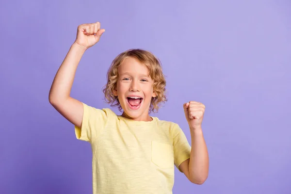 Foto de encantado menino levantar punhos gritar usar camiseta amarela isolada sobre fundo cor violeta — Fotografia de Stock