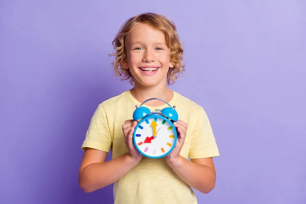 Foto de positivo alegre pequeno menino segurar relógio mostrar tempo isolado sobre cor violeta fundo — Fotografia de Stock