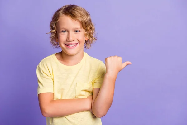 Foto positiver Junge zeigt Daumenfinger leeren Raum für Promo-Werbung tragen gelbes T-Shirt isoliert über violettem Hintergrund — Stockfoto