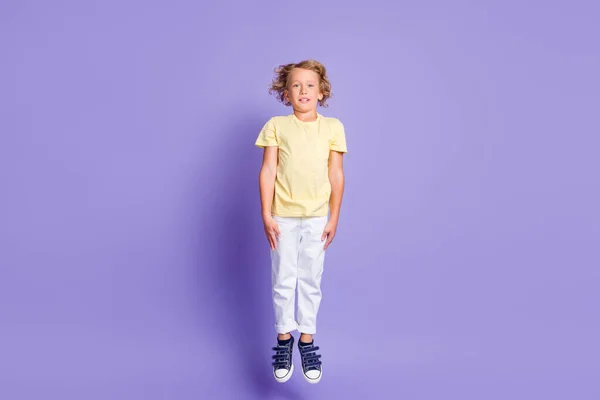 Фотографія повного розміру чарівного хлопчика, що стрибає вгору, одягаються в повсякденний стиль кросівки ізольовані на пастельному фіолетовому кольоровому фоні — стокове фото