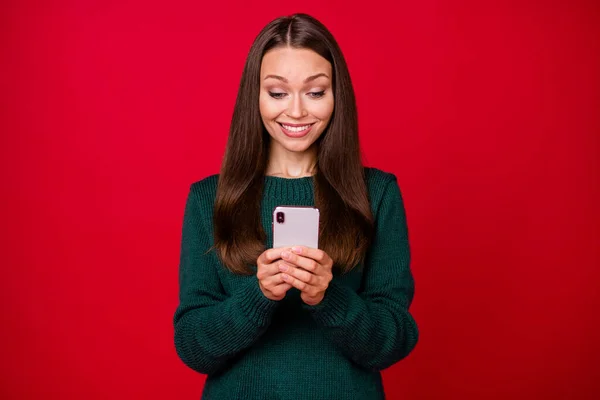 照片显示，智能手机上有一个积极的女孩穿着针织毛衣在明亮的红色背景下打字 — 图库照片