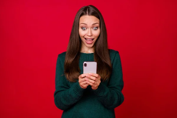 Фотографія божевільної дівчини, яку читають на смартфоні Різдвяні привітання носять зелений пуловер ізольовано на яскраво-червоному кольоровому фоні — стокове фото