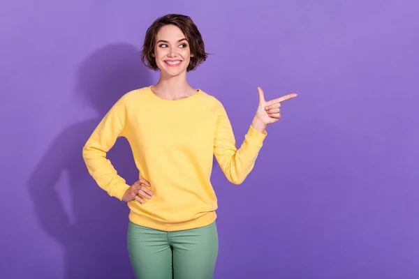 Photo of positive girl point finger look empty space wear green trousers yellow pullover isolated on violet color background — Stock Photo, Image
