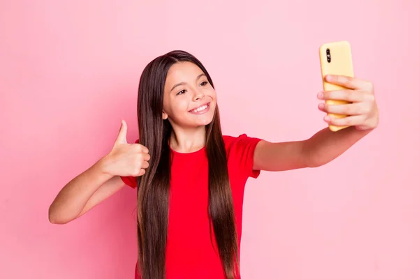 Foto de linda encantadora dama pequeña larga peinado levantar la mano sostener el teléfono mostrar el pulgar hacia arriba hacer selfie toothy radiante sonrisa usar casual elegante camiseta roja aislado color rosa fondo —  Fotos de Stock