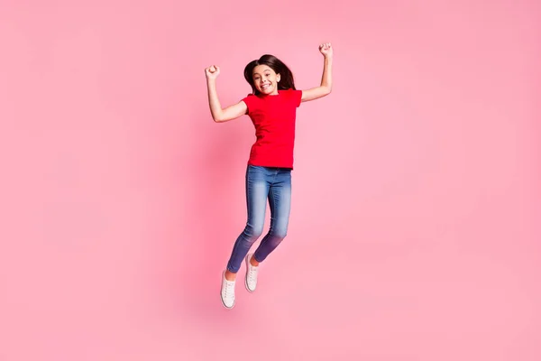 Ganzes Foto von fröhlichen Kind Mädchen springen heben Fäuste tragen rote lässige T-Shirt isoliert über pastellfarbenen Hintergrund — Stockfoto