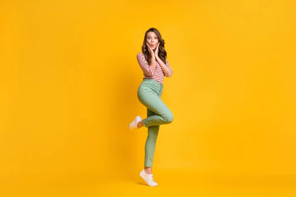 Longitud completa tamaño del cuerpo foto de la niña de pie de puntillas sorprendida tocando pómulos aislados sobre fondo de color amarillo brillante —  Fotos de Stock