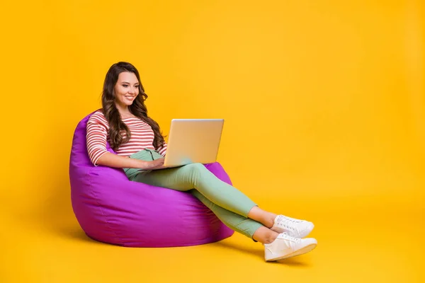 Tamanho total do corpo perfil lateral foto menina sentada em cadeira de feijão com laptop isolado no fundo de cor amarelo brilhante com copyspace — Fotografia de Stock