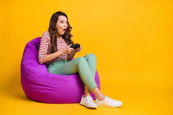 全身型侧写照片女孩坐在椅子上玩电子游戏，用鲜活的黄色背景与空旷的空间隔开 — 图库照片