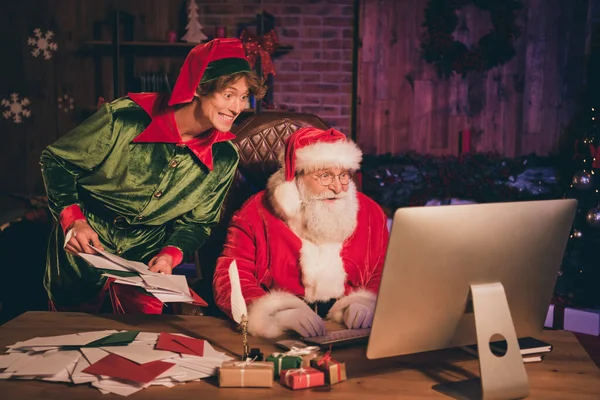 Фотопортрет Санта-Клауса и эльфа, смотрящего на экран компьютера с буквами — стоковое фото