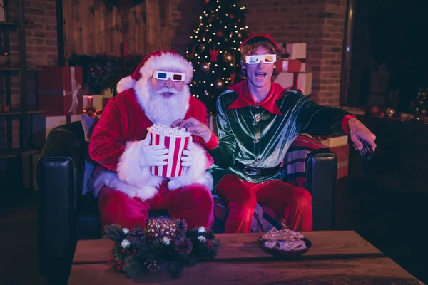 Zdjęcie portret Świętego Mikołaja i elfa jedzących popcorn przy użyciu zdalnego oglądania filmu na sofie w okularach 3D — Zdjęcie stockowe