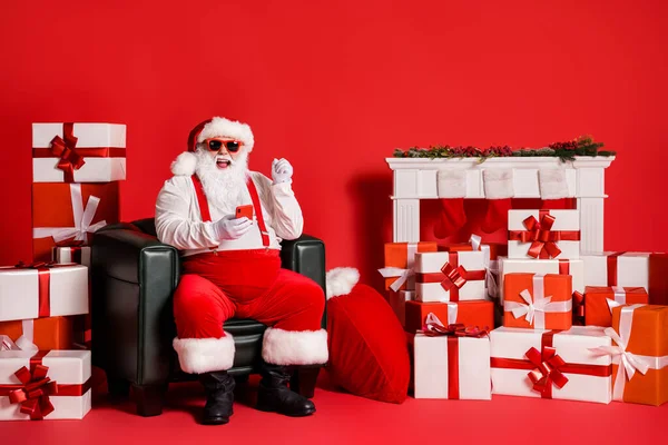 Retrato de su agradable atractivo funky grasa alegre alegre Santa usando aplicación gadget 5g blogging sentado en sillón divertirse aislado sobre brillante brillo vivo vibrante color rojo fondo —  Fotos de Stock