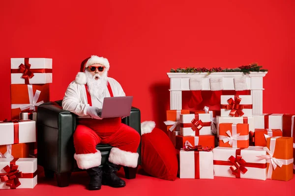 Retrato dele ele agradável atraente gordura funky espantado atordoado Santa usando laptop sentado em pilha poltrona pilha presentes ordem leitura e-mail isolado brilhante brilhante brilho vibrante cor vermelha fundo — Fotografia de Stock