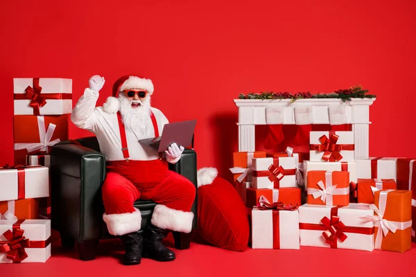 Retrato de su agradable atractivo funky grasa alegre alegre suerte Santa usando portátil sentado en sillón tienda de regocijo descuento aislado brillante brillo vivo vibrante color rojo fondo —  Fotos de Stock