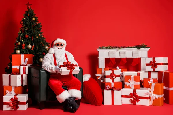 Portret van zijn hij mooie aantrekkelijke funky vet vrolijke vrolijke Santa vader zitten in fauteuil vasthouden in handen geven geschenk levering stapel stapel geïsoleerde heldere levendige glans levendige rode kleur achtergrond — Stockfoto