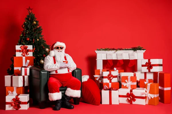 Portret van zijn hij mooie aantrekkelijke funky vet overgewicht vrolijke Kerstman zitten in fauteuil drinken drank in ingerichte kamer geïsoleerde heldere levendige glans levendige rode kleur achtergrond — Stockfoto