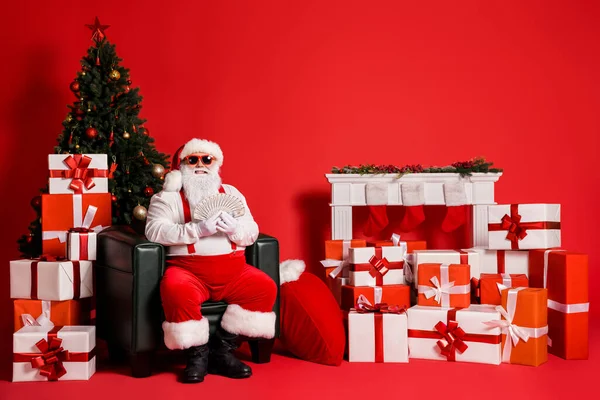 Porträt seiner er schön attraktiv funky Fett fröhlich reich Weihnachtsmann Vater sitzt im Sessel hält in den Händen Bündel Bargeld uns Gewinn isoliert hell lebendigen Glanz leuchtenden roten Hintergrund — Stockfoto