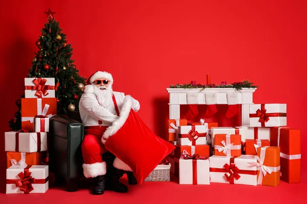 Retrato de su atractivo grasa funky sobrepeso alegre alegre Santa sentado en sillón preparando cajas de regalo de embalaje en el saco Eve Noel aislado brillo vivo brillante vibrante color rojo fondo —  Fotos de Stock