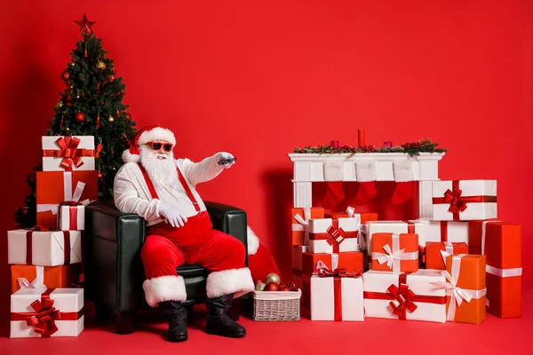 Portret jego atrakcyjny funky tłuszczu otyłość wesoły Mikołaj siedzi w fotelu oglądając TV film cieszący się odpoczynku w salonie odizolowany jasny żywy blask żywy czerwony kolor tło — Zdjęcie stockowe